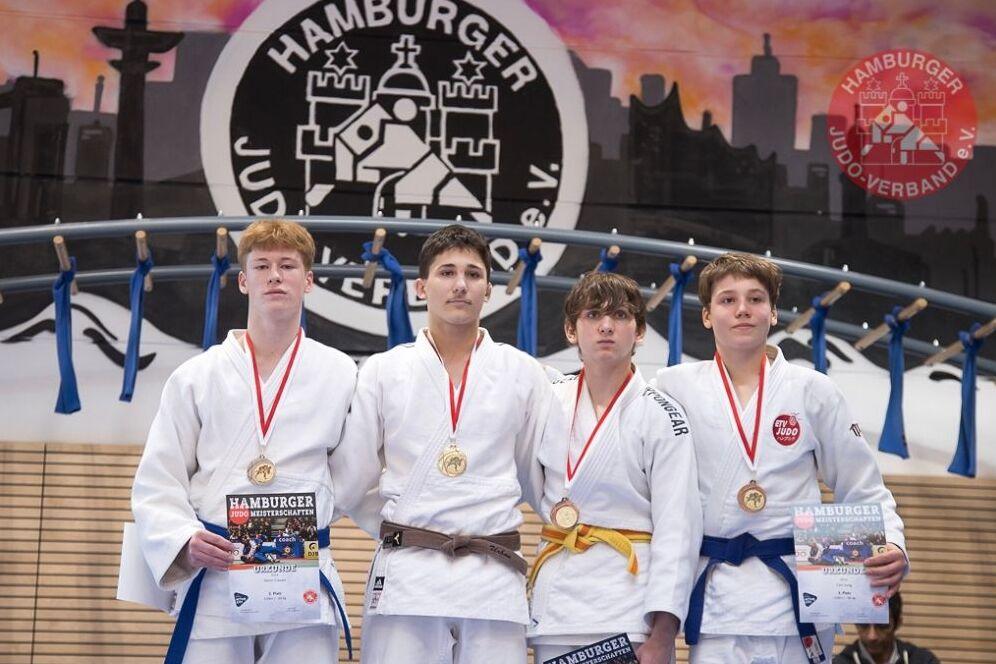 Vier Judokas in wei&szlig;en Anz&uuml;gen mit Medaillen stehen auf einem Podium, halten Urkunden vor einem bunten Hintergrund.