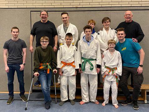 Gruppenfoto von neun Personen in judowhiten Anzügen mit verschiedenen Gürtelfarben in einer Sporthalle.