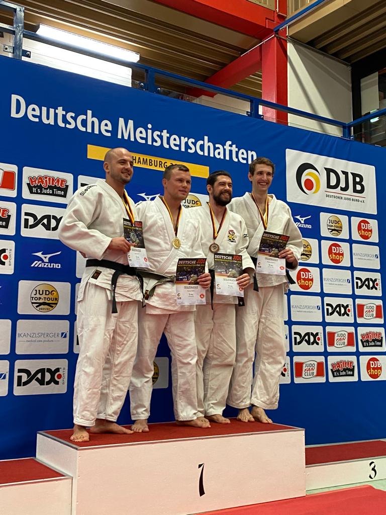 Vier Judoka in weißen Anzügen stehen auf dem Siegertreppchen der Deutschen Meisterschaften und halten Medaillen und Urkunden.