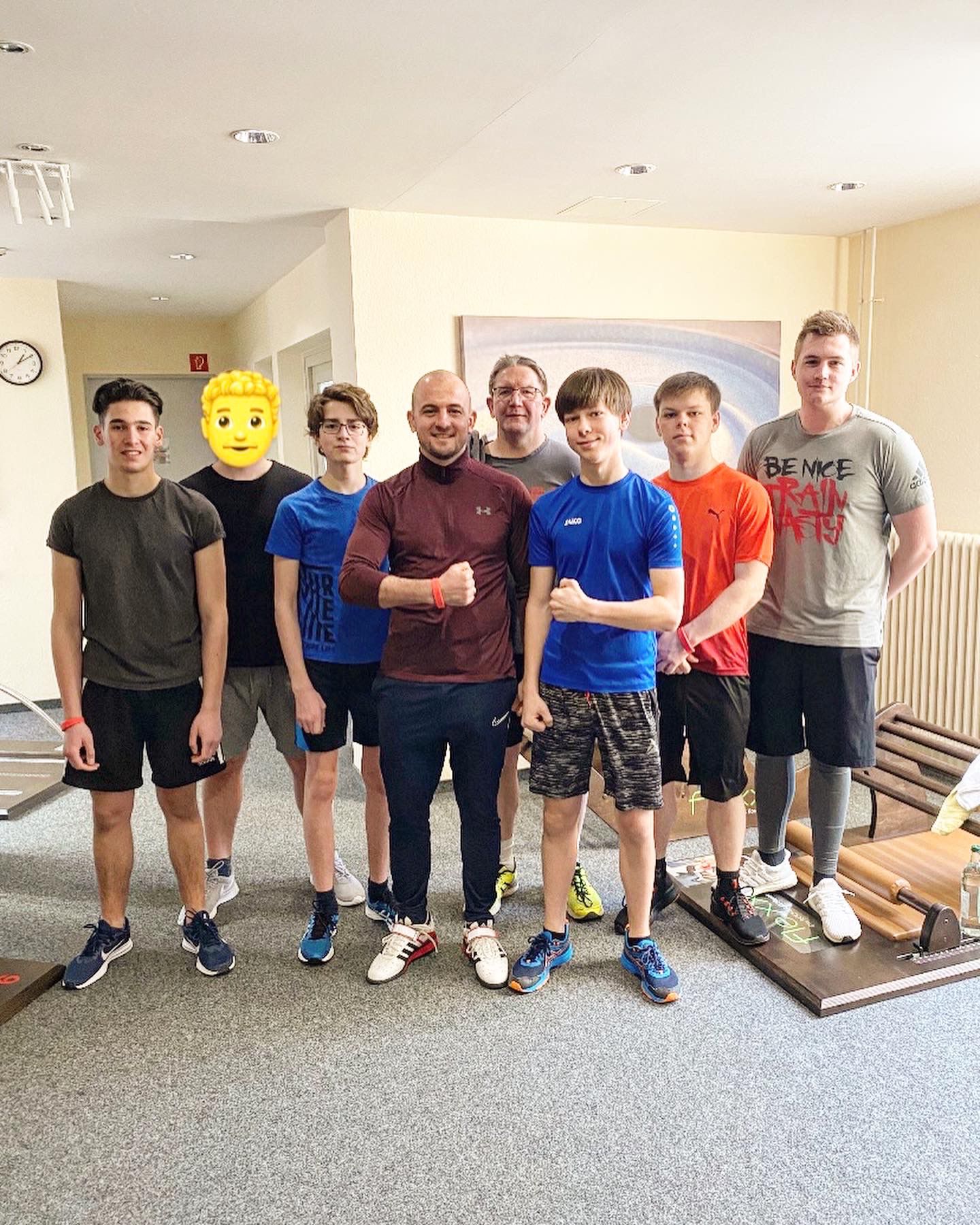Gruppe von sechs Jugendlichen und einem Trainer in Sportkleidung, lächeln in einem Raum mit Fitnessgeräten.