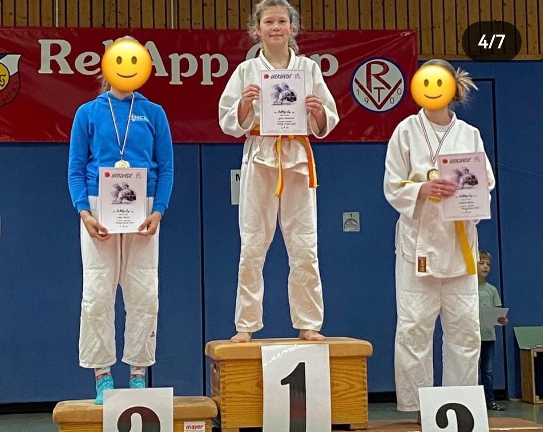Drei Kinder in Judokleidung erhalten Urkunden auf einem Siegerpodest bei einem Wettkampf.