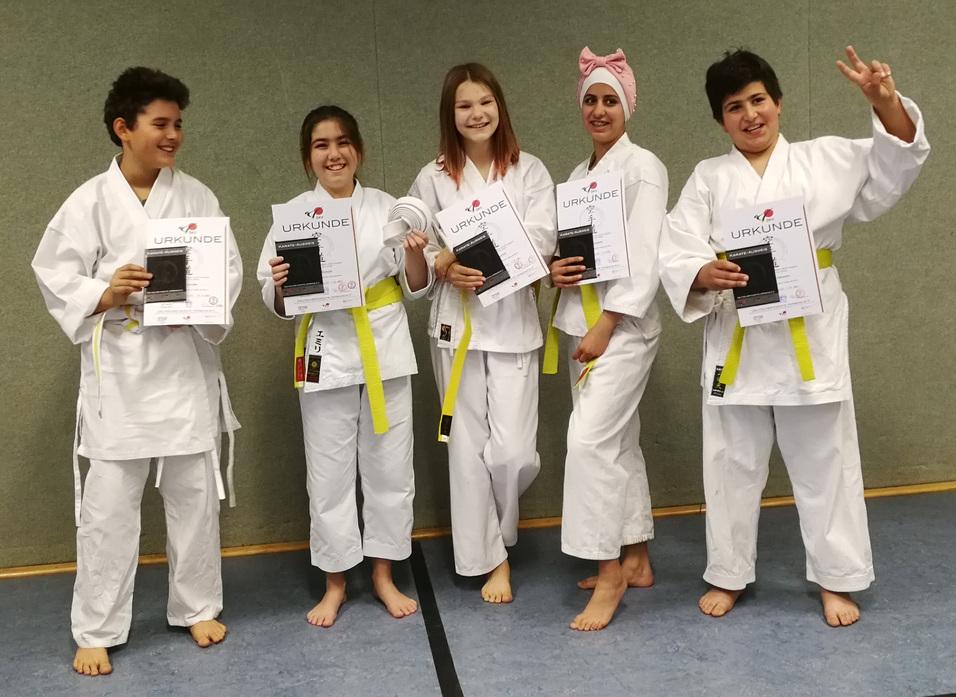 Fünf Kinder in Karate-Anzügen zeigen stolz ihre Urkunden für bestandene Prüfungen.
