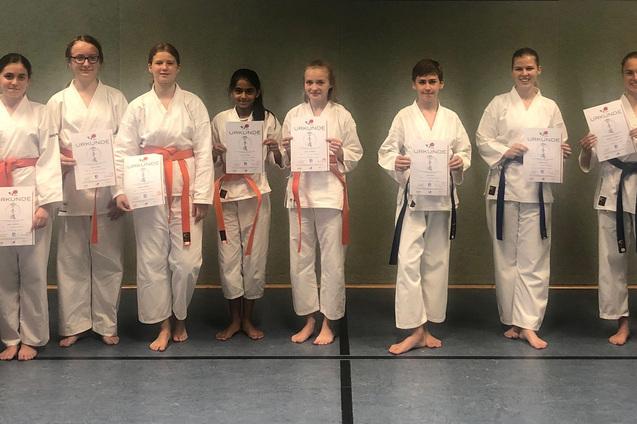 Gruppe von Karateka in Dojo-Uniformen, die stolz ihre Urkunden nach einer Veranstaltung pr&auml;sentieren.