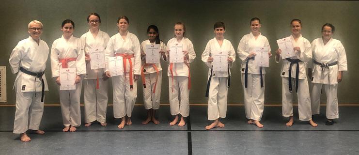 Gruppe von Karateka in Dojo-Uniformen, die stolz ihre Urkunden nach einer Veranstaltung präsentieren.