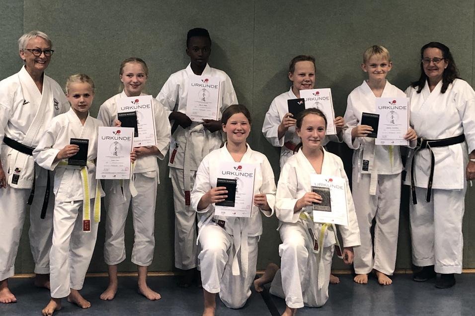 Gruppenfoto von Karateka in wei&szlig;em Gi, die Urkunden in den H&auml;nden halten, im Hintergrund eine gr&uuml;ne Wand.