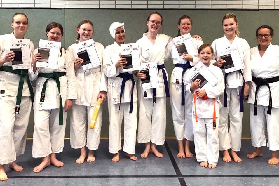 Gruppe von Karateka in wei&szlig;en Gi mit Urkunden, die Erfolge feiern, stehen barfu&szlig; auf einer Matte.