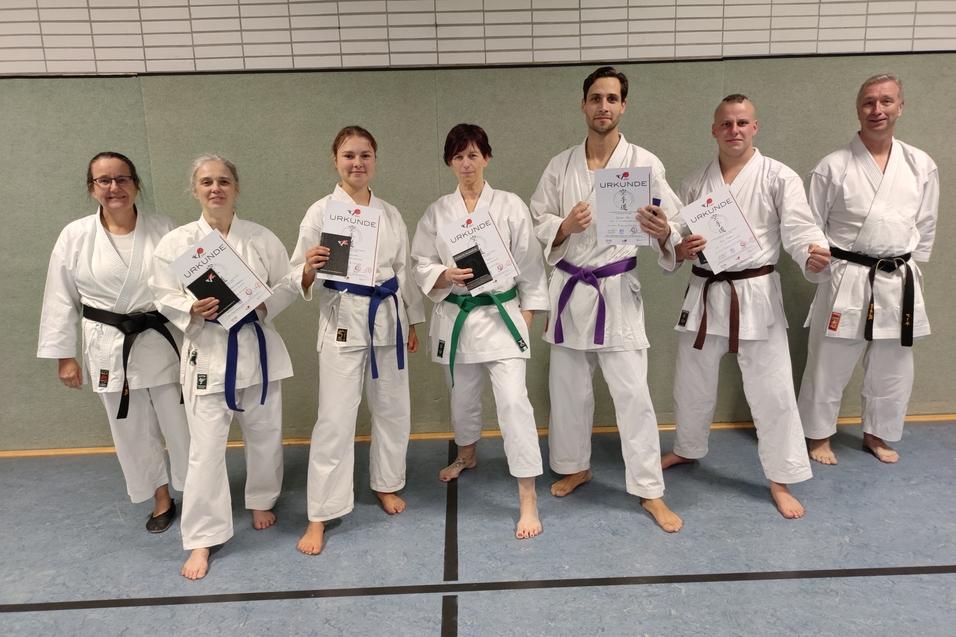 Gruppe von Karateka in wei&szlig;em Gi h&auml;lt Urkunden, stehen auf einer Matte in einer Sporthalle.