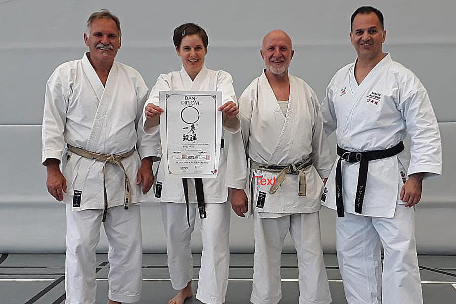Prüfung 2023 - DAN Sonja Vier Karateka in weißen Trainingsanzügen posieren gemeinsam mit einem Dan-Diplom auf einer Matte.