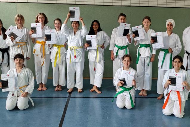 Gruppenszene von Karateka in wei&szlig;en Gi, die stolz ihre Urkunden in der Sporthalle halten. Farbige G&uuml;rtel sichtbar.