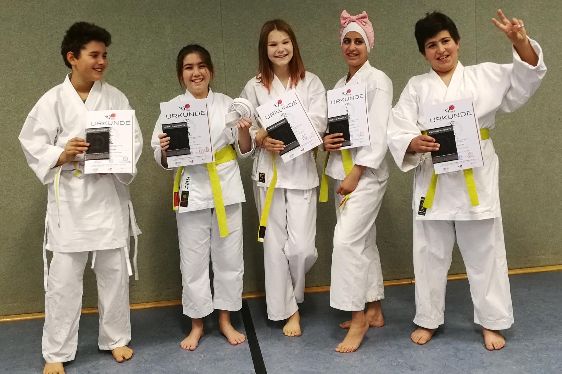 F&uuml;nf Kinder in Karate-Anz&uuml;gen zeigen stolz ihre Urkunden f&uuml;r bestandene Pr&uuml;fungen.