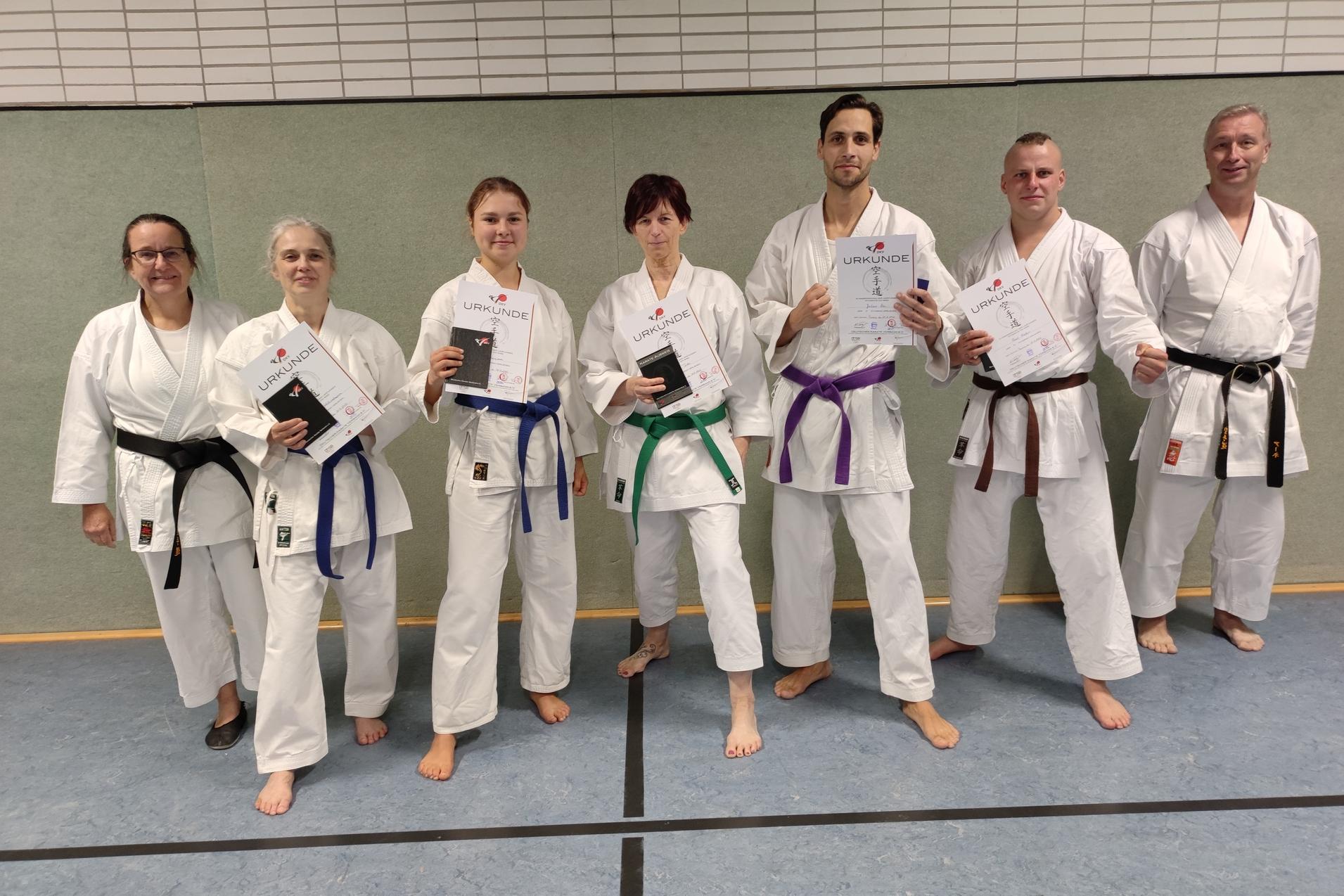 Gruppe von Karateka in wei&szlig;em Gi h&auml;lt Urkunden, stehen auf einer Matte in einer Sporthalle.