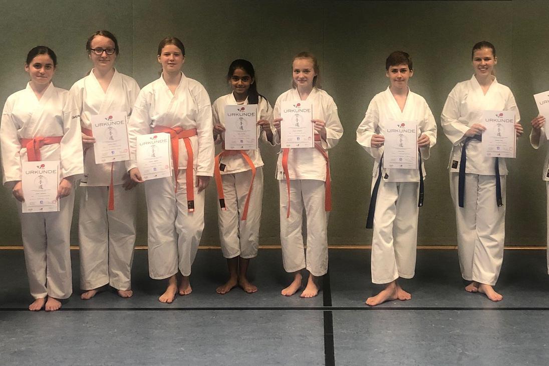 Gruppe von Karateka in Dojo-Uniformen, die stolz ihre Urkunden nach einer Veranstaltung pr&auml;sentieren.