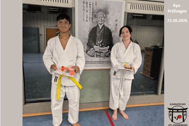 Kyu-Prüfungen Zwei Prüflinge in weißen Karateanzügen mit gelbem und weißem Gürtel stehen in einer Sporthalle vor einem großen Funakoshi-Bild und halten Urkunden und kleine Geschenke