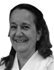 Portrait einer lächelnden Frau mit langen, lockigen Haaren, gekleidet in einen weißen Karate-Gi.