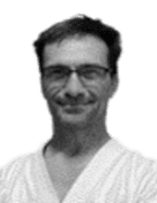 Porträt eines lächelnden Mannes mit Brille, getragenem weißen Karate-Gi und kurzem Haar.
