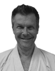 Lächelnder Mann in Karate-Uniform vor einfarbigem Hintergrund.
