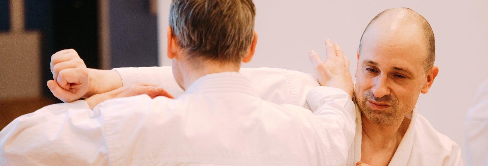 In einer Nahaufnahme f&uuml;hren zwei M&auml;nner in wei&szlig;en Karateanz&uuml;gen eine Kampftechnik durch