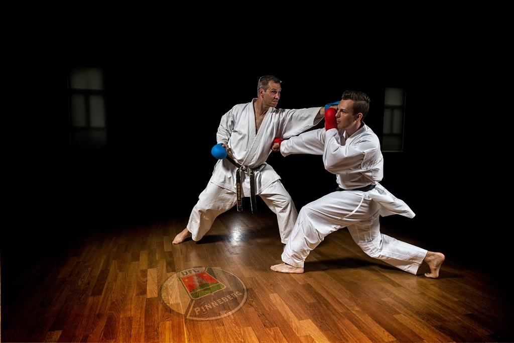 Zwei Karatek&auml;mpfer in wei&szlig;en Anz&uuml;gen &uuml;ben Techniken auf einem Holzboden in einem dunklen Raum.