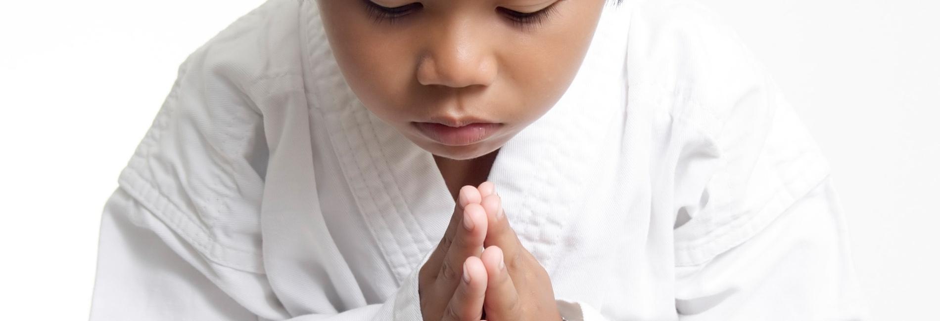 Junger Karateka mit gelbem Gürtel, der mit gefalteten Händen und gesenktem Kopf eine respektvolle Geste zeigt.