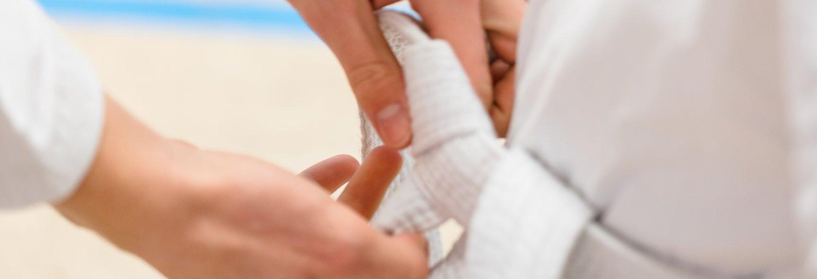 H&auml;nde binden einen wei&szlig;en G&uuml;rtel um die Taille einer Person in wei&szlig;em Karateanzug