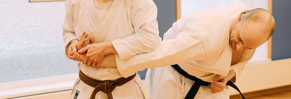 In einer Nahaufnahme f&uuml;hren zwei M&auml;nner in wei&szlig;en Karateanz&uuml;gen eine Kampftechnik durch