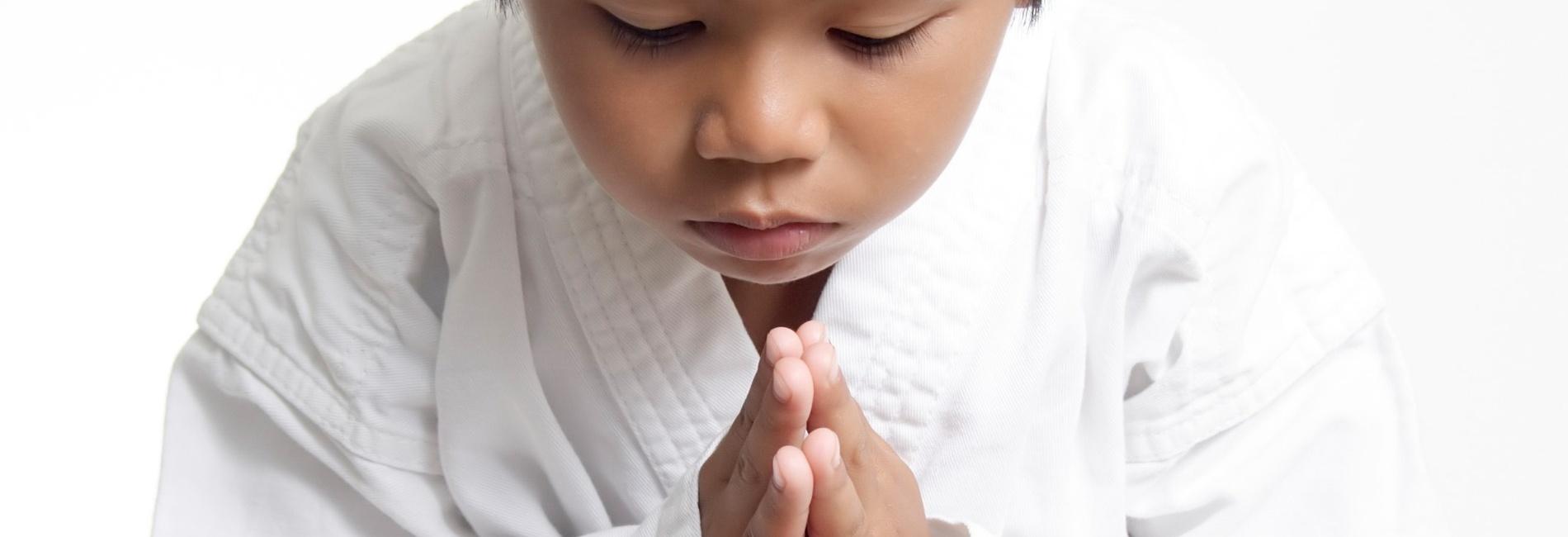 Junger Karateka mit gelbem G&uuml;rtel, der mit gefalteten H&auml;nden und gesenktem Kopf eine respektvolle Geste zeigt.