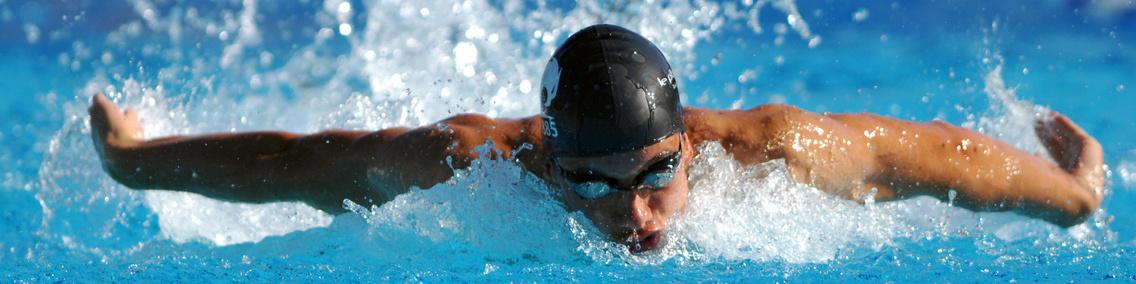 Schwimmer in Schwimmkappe und Brille führt einen Schmetterlingsschwimmzug in einem blauen Becken aus.