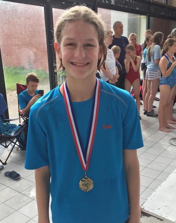 Junge mit Medaille und breitem Lächeln, steht in einem Schwimmbad neben anderen Kindern in Badebekleidung.