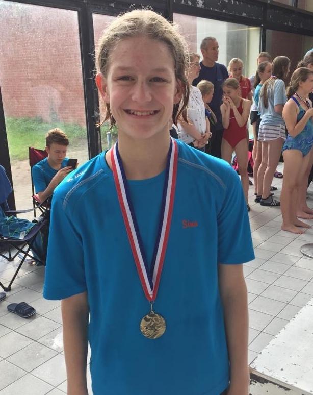 Junge mit Medaille und breitem L&auml;cheln, steht in einem Schwimmbad neben anderen Kindern in Badebekleidung.