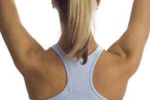 R&uuml;ckansicht einer Person mit h&auml;ngendem Haar, die in einem blauen Sporttop steht und die Arme nach oben hebt.