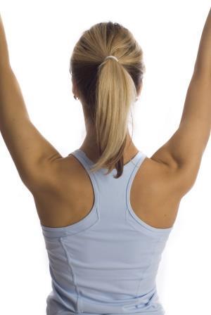 Rückansicht einer Person mit hängendem Haar, die in einem blauen Sporttop steht und die Arme nach oben hebt.