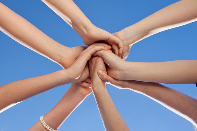 Verschr&auml;nkte H&auml;nde von mehreren Personen vor einem klaren blauen Himmel bilden eine symbolische Einheit.