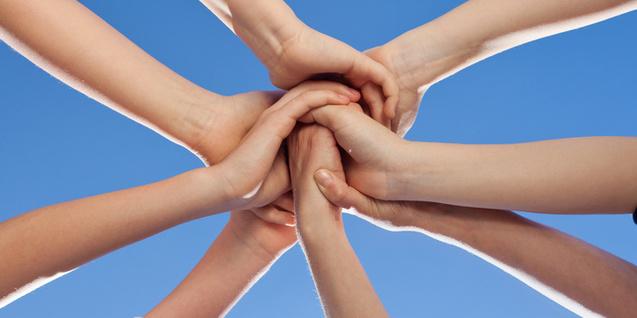 Verschränkte Hände von mehreren Personen vor einem klaren blauen Himmel bilden eine symbolische Einheit.