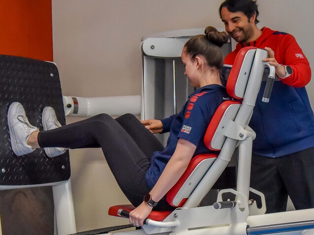 Eine Trainerin hilft einer Frauen beim Beintraining an einer Fitnessmaschine im Studio.