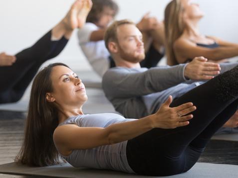 Gruppe von Menschen in Sportkleidung macht Pilates-&Uuml;bungen auf Matten in einem hellen Raum.