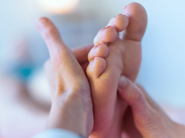 Nahaufnahme einer Hand, die eine Fußmassage an einem Fuß mit lackierten Nägeln durchführt. Hintergrund unscharf.