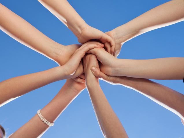 Verschränkte Hände von mehreren Personen vor einem klaren blauen Himmel bilden eine symbolische Einheit.