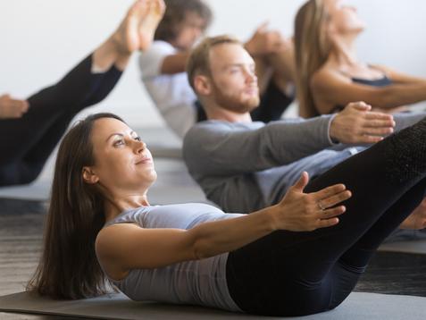 Gruppe von Menschen in Sportkleidung macht Pilates-Übungen auf Matten in einem hellen Raum.