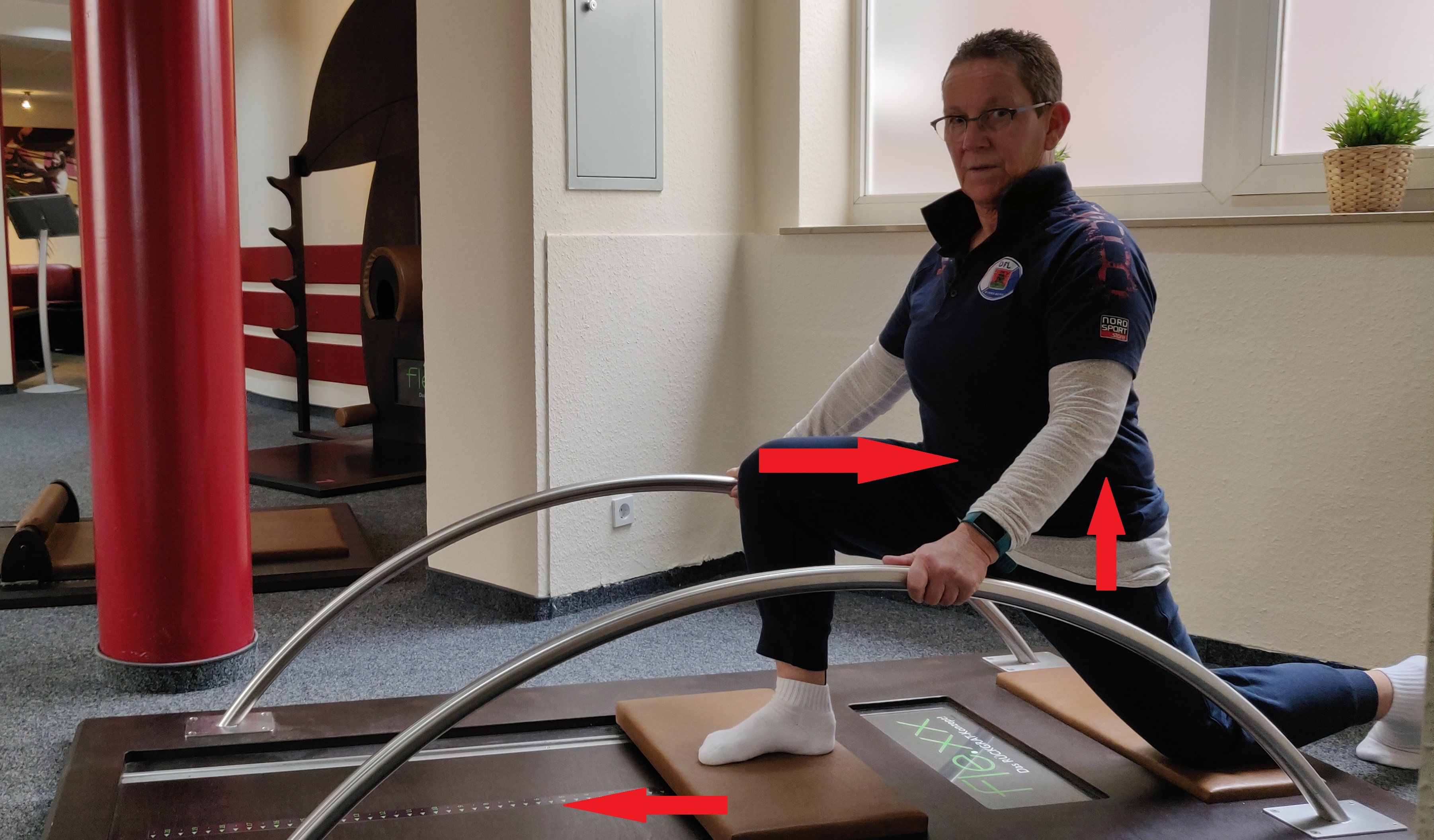 Frau in Sportkleidung macht eine Übung auf einem Trainingsgerät in einem Fitnessraum.