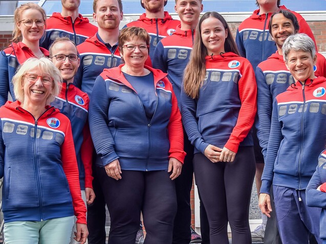 Gruppenaufnahme von elf Personen in einheitlichen Jacken, die auf Treppenstufen vor einem Gebäude stehen.