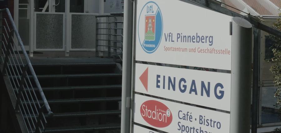 Eingangsbereich des VfL Pinneberg mit einem Informationsschild und Stufen zur Eingangstür des Sportzentrums.