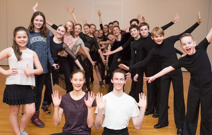 Gruppe junger Tänzer in Pose, lächelnd, in einem Tanzstudio mit Holzfußboden.