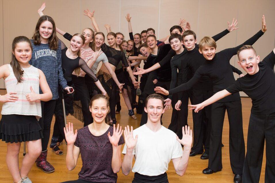Gruppe junger T&auml;nzer in Pose, l&auml;chelnd, in einem Tanzstudio mit Holzfu&szlig;boden.