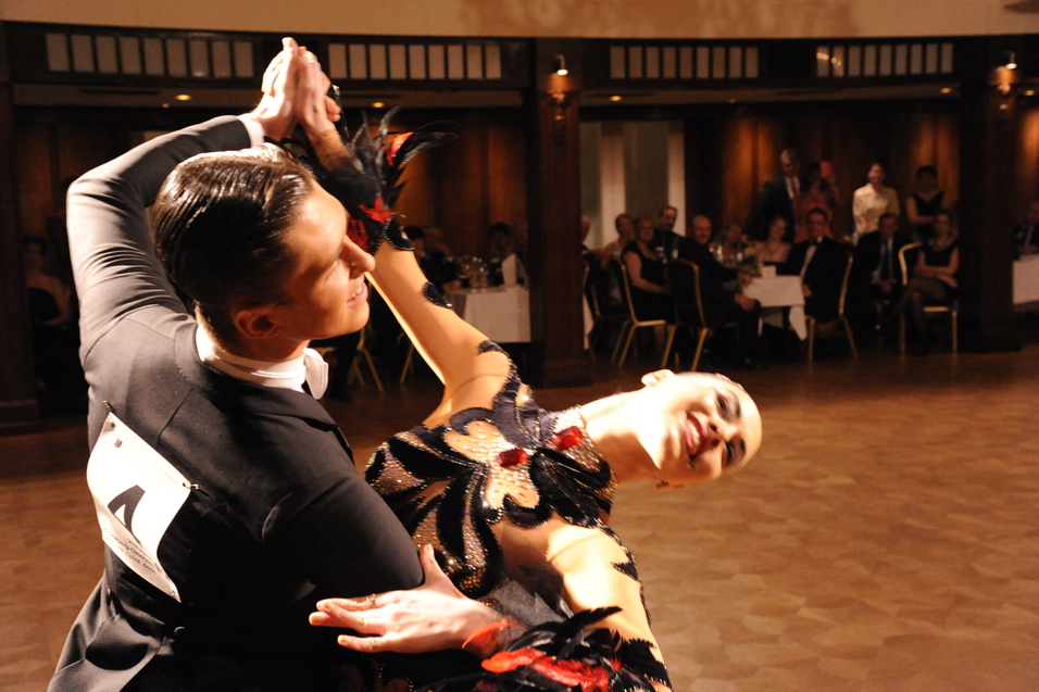 Tanzpaar in Aktion bei einem Wettbewerb, umgeben von Publikum in eleganter Abendkleidung.