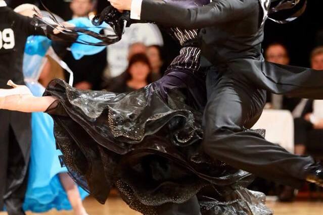 Tanzendes Paar in eleganter Kleidung, M&auml;nner im Anzug, Frauen in schwarzem Kleid, auf einer Tanzfl&auml;che w&auml;hrend eines Wettbewerbs.