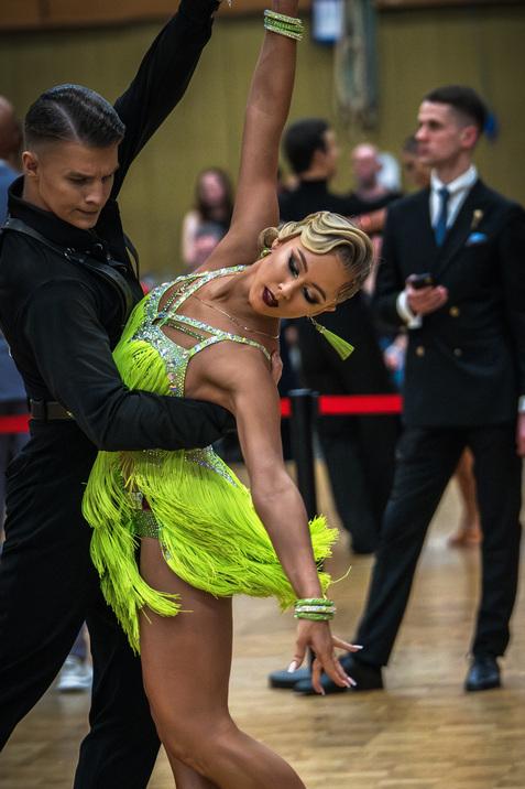 Tanzpaar in der Bewegung: Frau in leuchtend gr&uuml;ner Kost&uuml;m mit Fransen, Mann in schwarzem Outfit. Wettbewerbsumgebung.