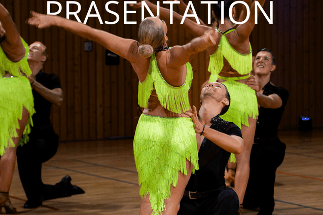 Tanzende Paare in grellen, fransigen Outfits auf einer Holzbodenfl&auml;che w&auml;hrend einer Tanzpr&auml;sentation.