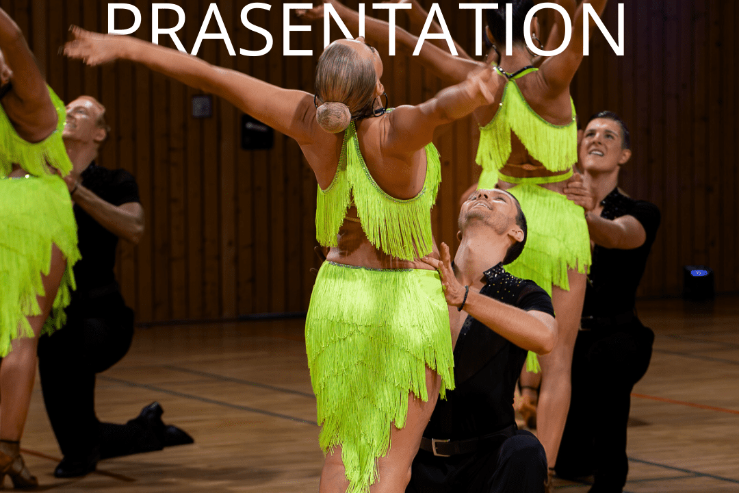 Tanzende Paare in grellen, fransigen Outfits auf einer Holzbodenfl&auml;che w&auml;hrend einer Tanzpr&auml;sentation.