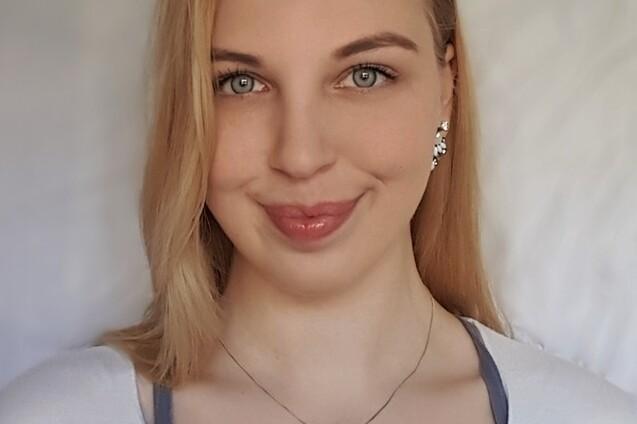 Portr&auml;t einer Frau mit blonden Haaren, die ein helles Oberteil tr&auml;gt, vor einem neutralen Hintergrund.