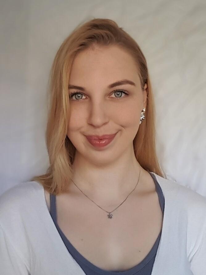 Porträt einer Frau mit blonden Haaren, die ein helles Oberteil trägt, vor einem neutralen Hintergrund.